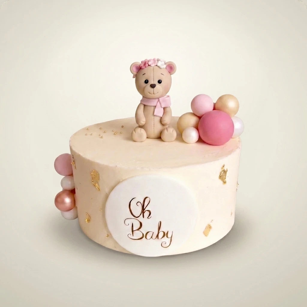 Tort na baby shower dla dziewczynki - kremowy tort z misiem z masy cukrowej w różowym wianku, różowo-złotymi kulami, złotymi płatkami i plakietką Oh Baby