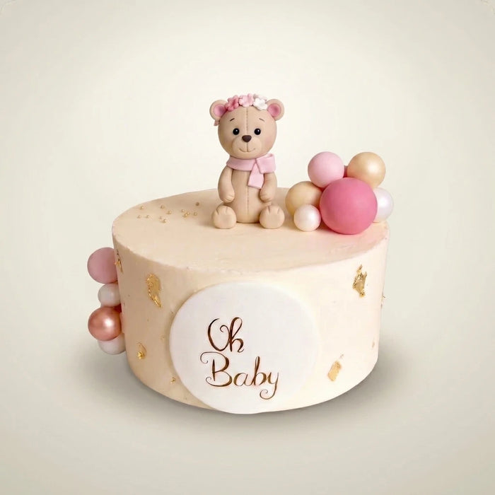 Tort na baby shower dla dziewczynki - kremowy tort z misiem z masy cukrowej w różowym wianku, różowo-złotymi kulami, złotymi płatkami i plakietką Oh Baby