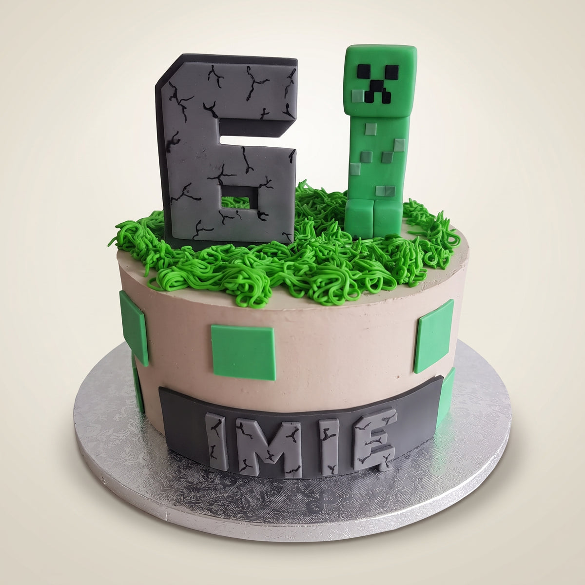 Tort Minecraft z Creeperem - kremowy tort z zieloną trawą z kremu, szarą cyfrą i figurką Creepera z masy cukrowej oraz ciemnym pasem z imieniem u dołu