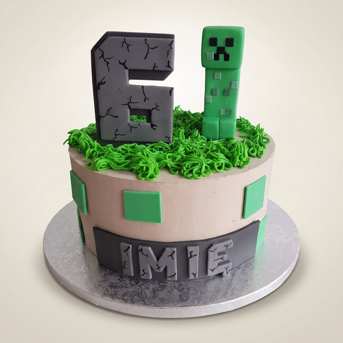 Tort Minecraft z Creeperem - kremowy tort z zieloną trawą z kremu, szarą cyfrą i figurką Creepera z masy cukrowej oraz ciemnym pasem z imieniem u dołu